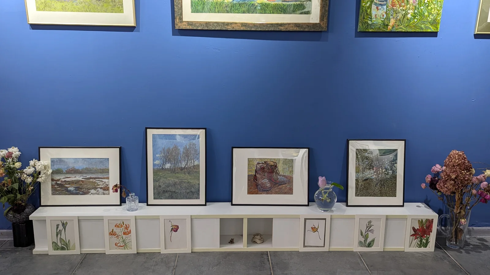 Картины и рисунки у синей стены выставочного зала